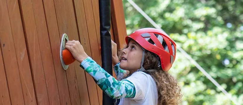 Girl in a red helmet climbs the Adventure tower at Camp Widjiwagan.